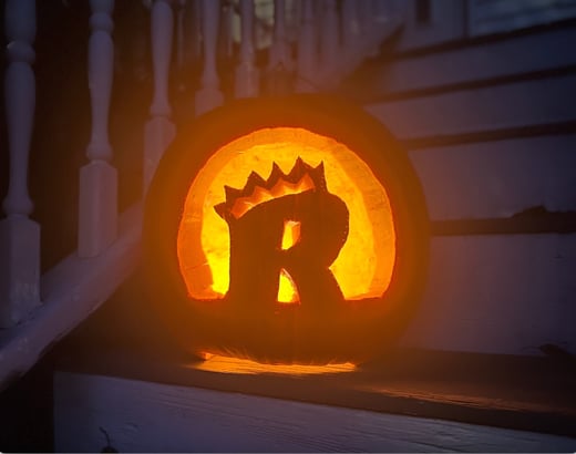 A lit jack-o-lantern with the Regis athletic logo carved into it
