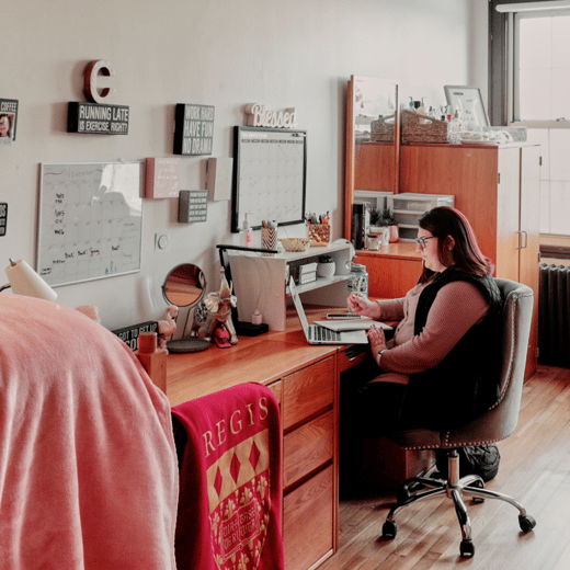 A student sitting at a desk in one of the Regis residence halls