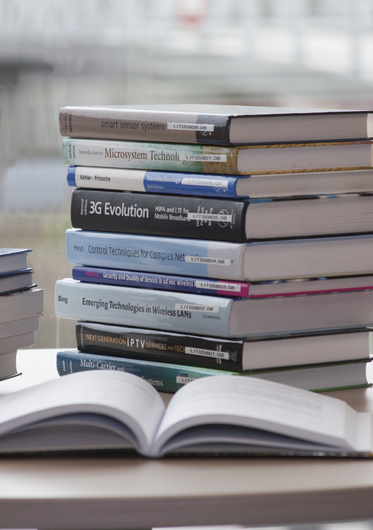 a stack of textbooks with one open text book in front